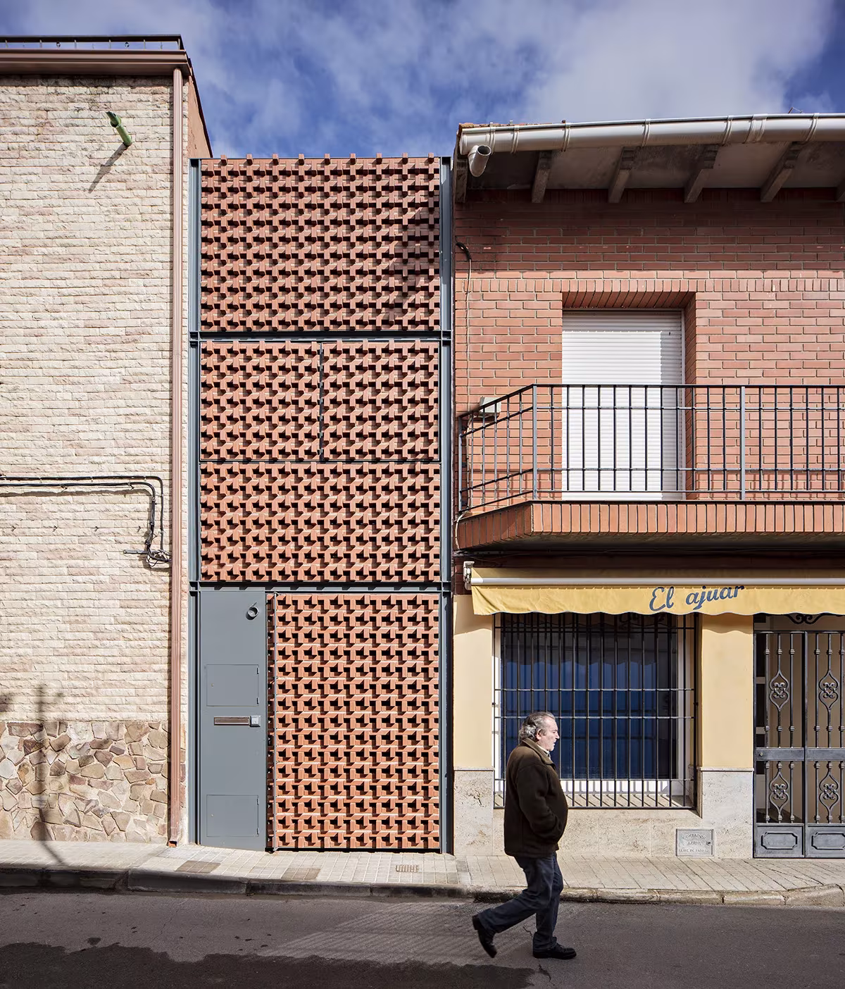Cortina de piezas cerámicas caladas y puerta gris junto al balcón vecino en la fachada de Casa Piedrabuena