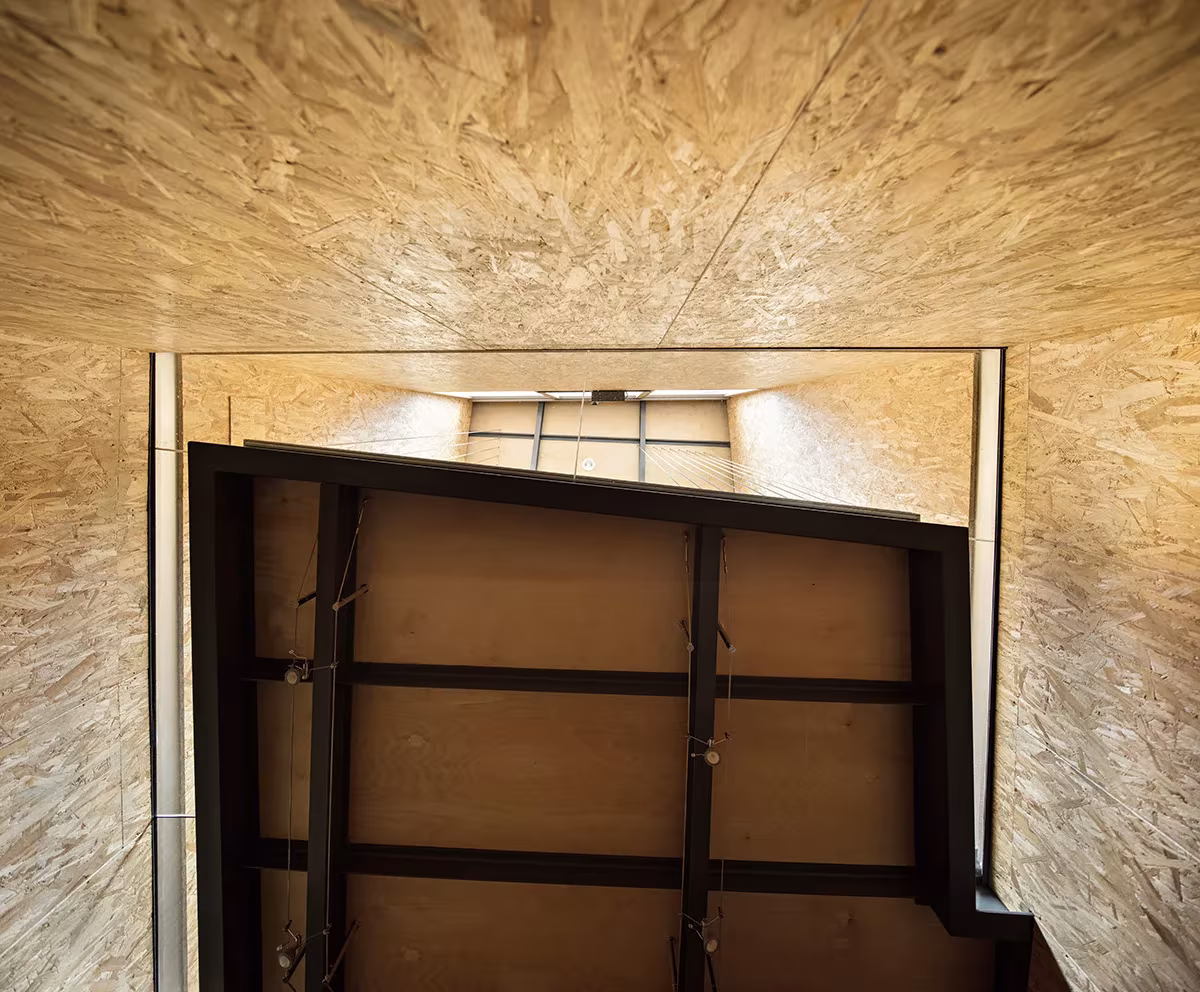 Panel pivotante de madera y acero abierto en un hueco entre paredes de OSB en Casa Piedrabuena