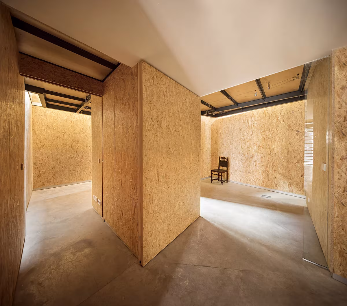 Estancia revestida de tableros OSB con un gran panel pivotante y una silla al fondo en Casa Piedrabuena