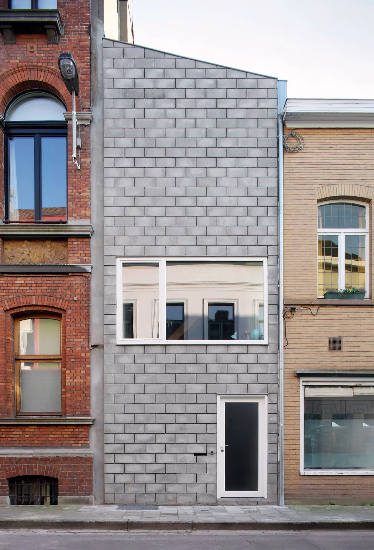 Fachada estrecha de bloque de hormigón gris entre edificios de ladrillo de la Casa 12k, en Gante, Bélgica