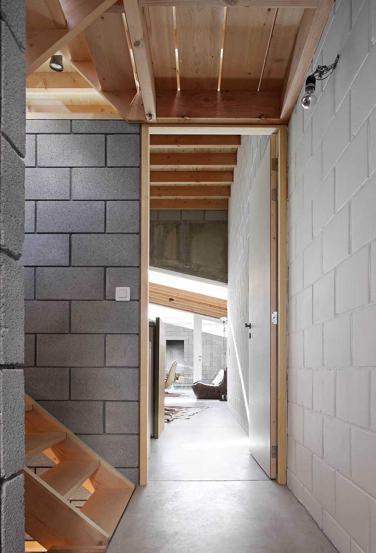 Pasillo de bloque gris con techo de madera hacia el salón luminoso de la Casa 12k, Gante