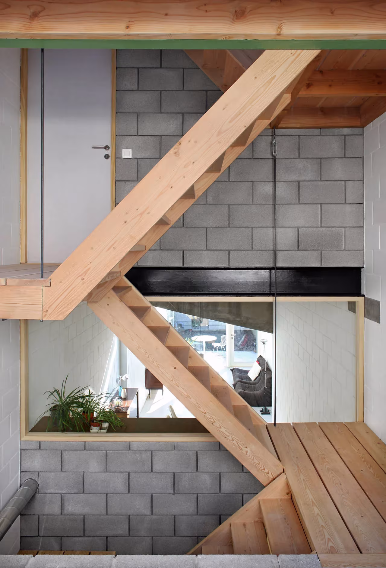 Escalera de madera de pino y muro de bloque de hormigón visto en el interior de la Casa 12k de Gante