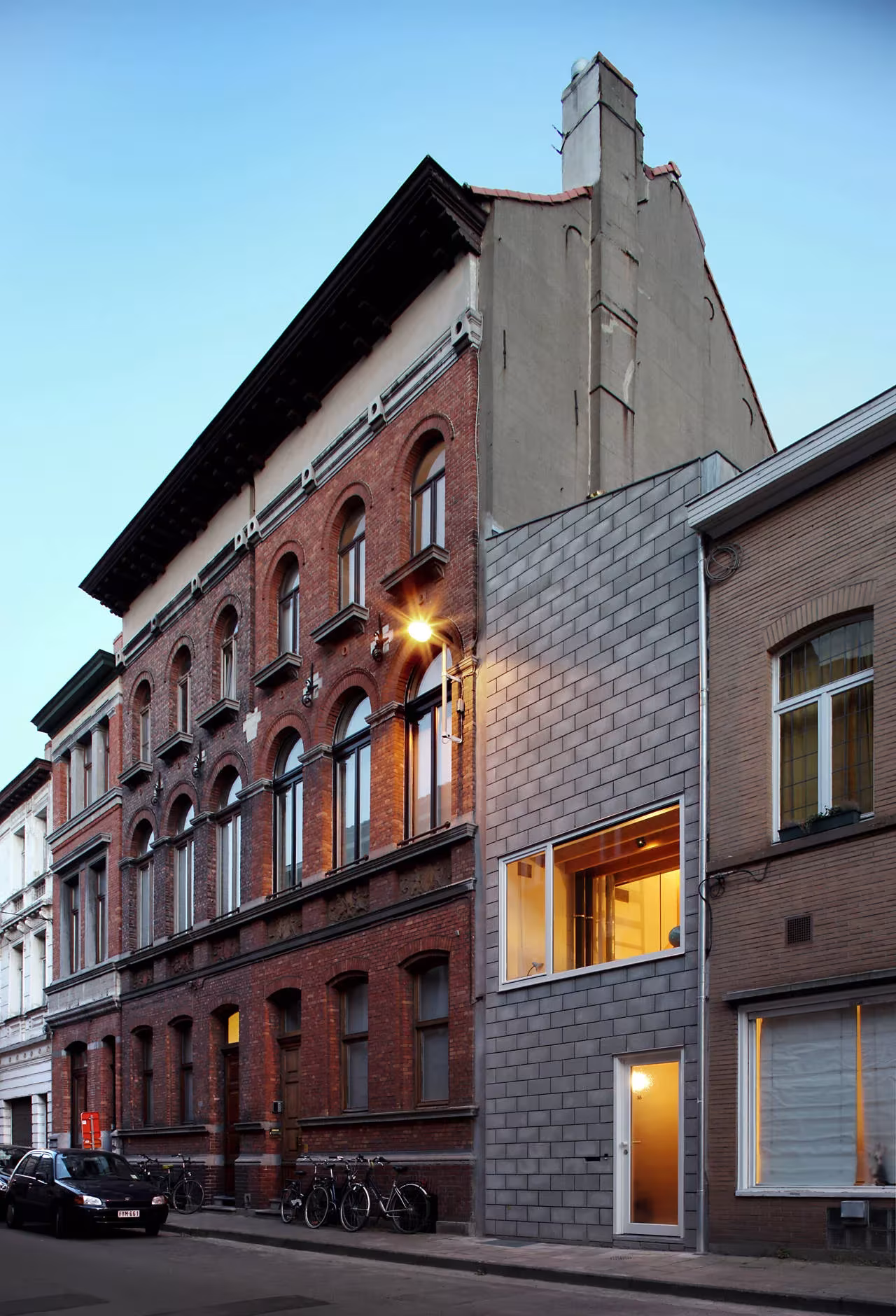 Casa 12k de bloque gris junto a un edificio de ladrillo rojo con ventanas en arco, en Gante, Bélgica