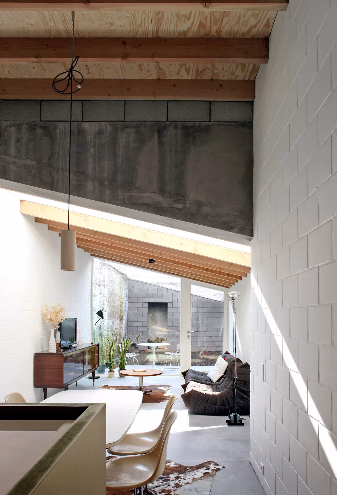 Salón de doble altura con lucernario, muro de bloque y mobiliario de diseño en la Casa 12k de Gante