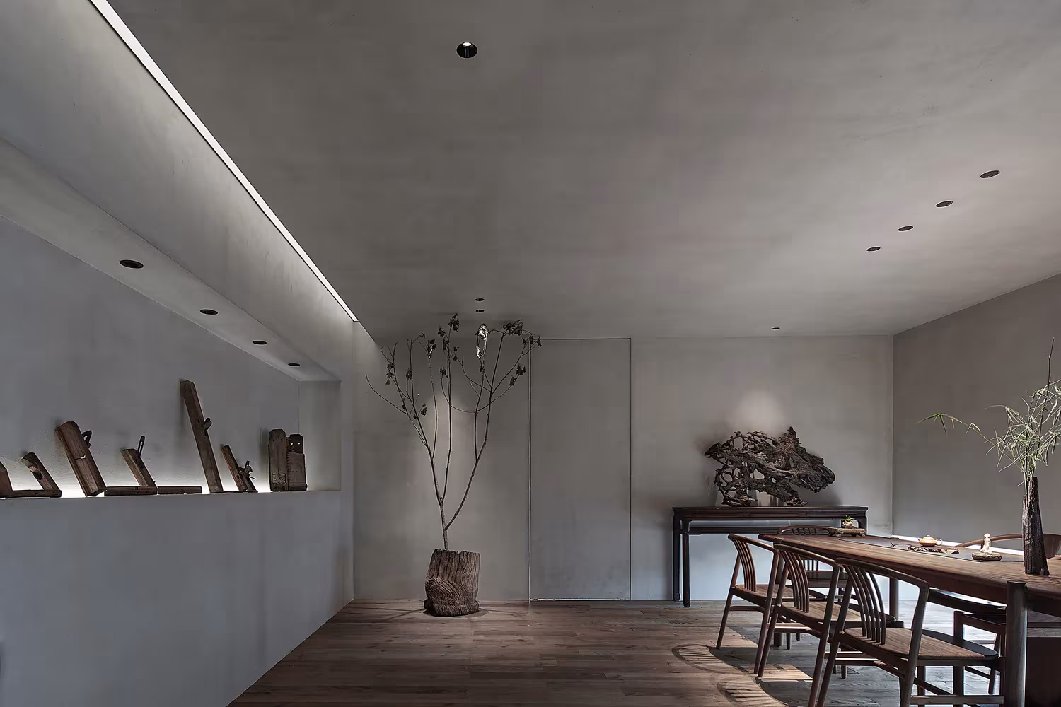 Estante de pared con piezas escultóricas y una rama de árbol junto a la mesa del Estudio Resee