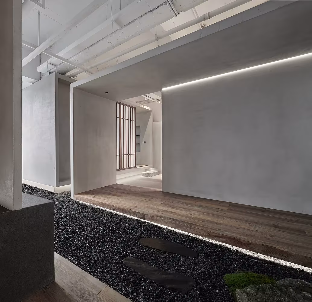 Pasaje entre muros de hormigón con jardín de grava, piedras y luz lineal en el Estudio Resee