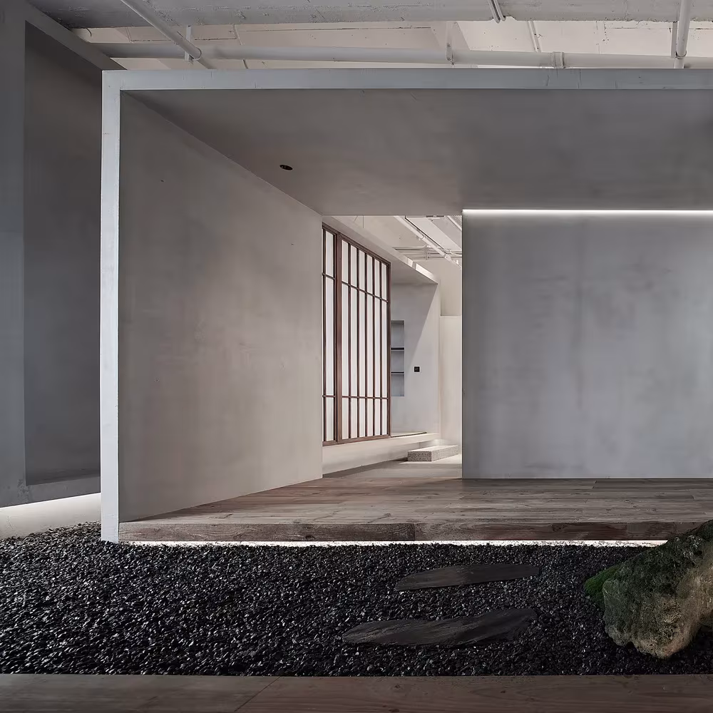 Umbral de hormigón gris con celosía de madera al fondo y lecho de grava negra en el Estudio Resee