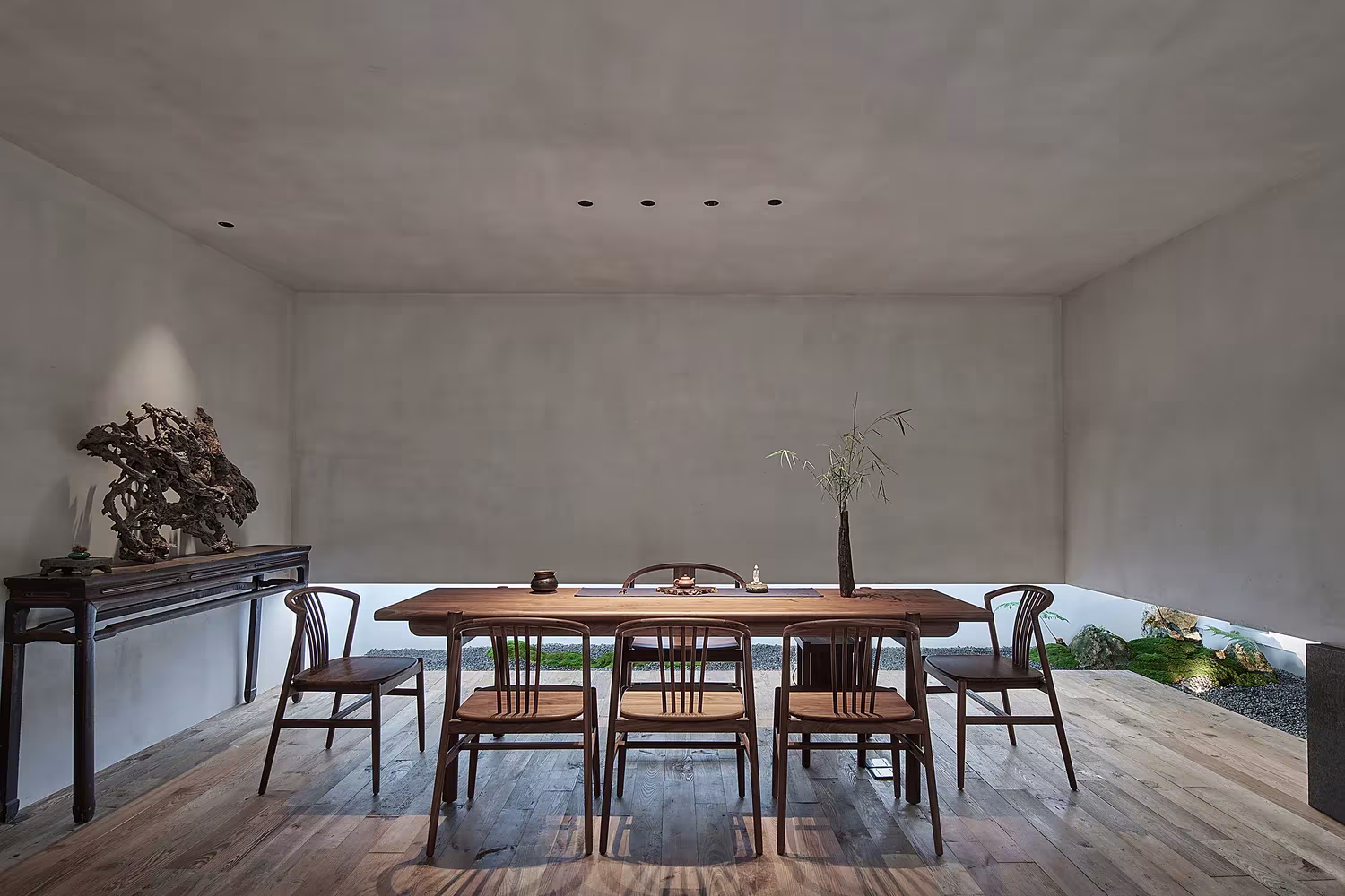 Mesa de té con sillas de madera y piedra escultórica ante un muro de microcemento en el Estudio Resee