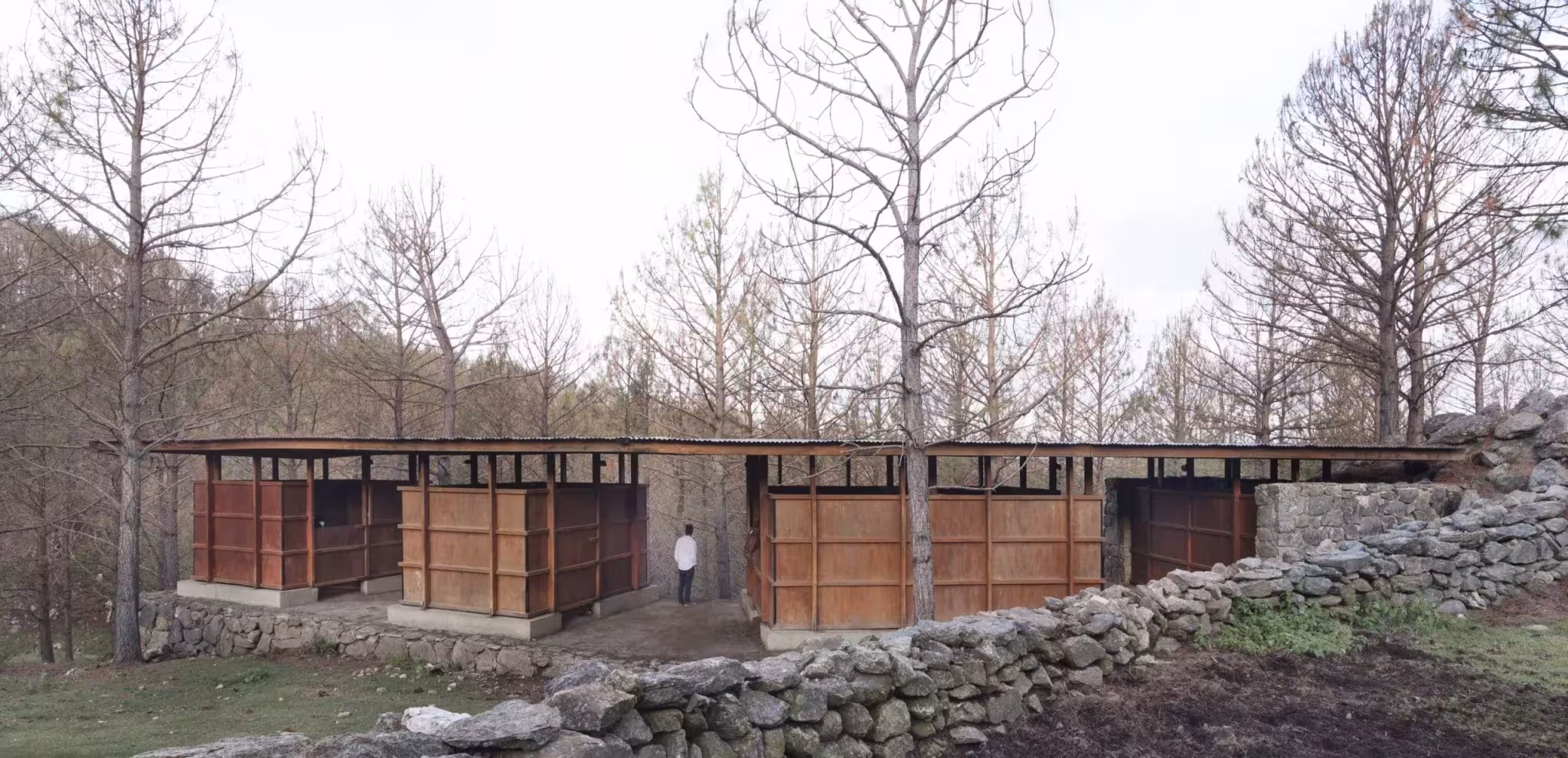 Frente de las Caballerizas CaRaJo con puertas de madera tras un muro bajo de piedra seca