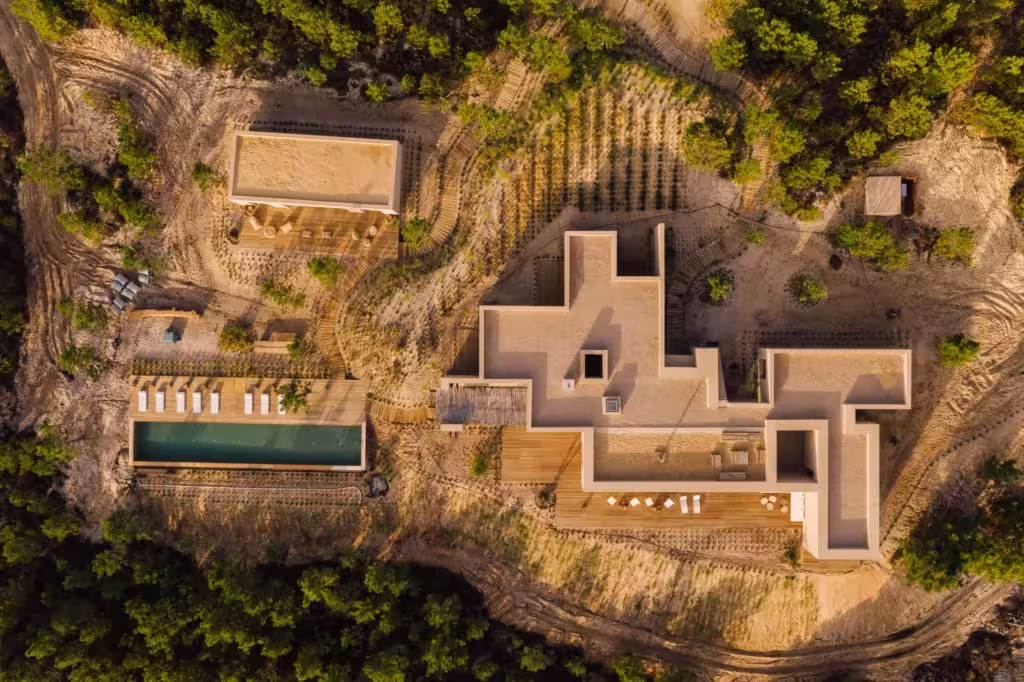 Vista aérea de Melides Art: volúmenes blancos escalonados y una piscina alargada entre pinos y tierra