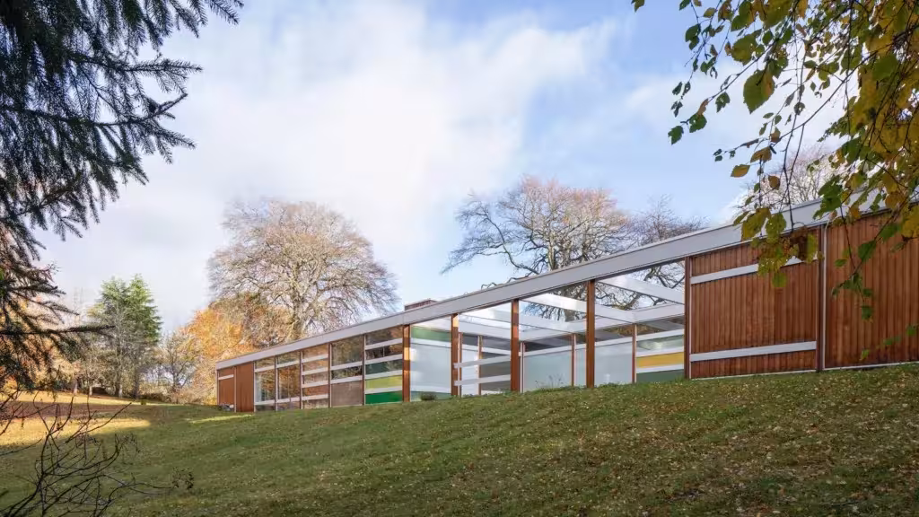 Casa High Sunderland, pabellón bajo con paneles de colores y madera sobre una pradera con árboles