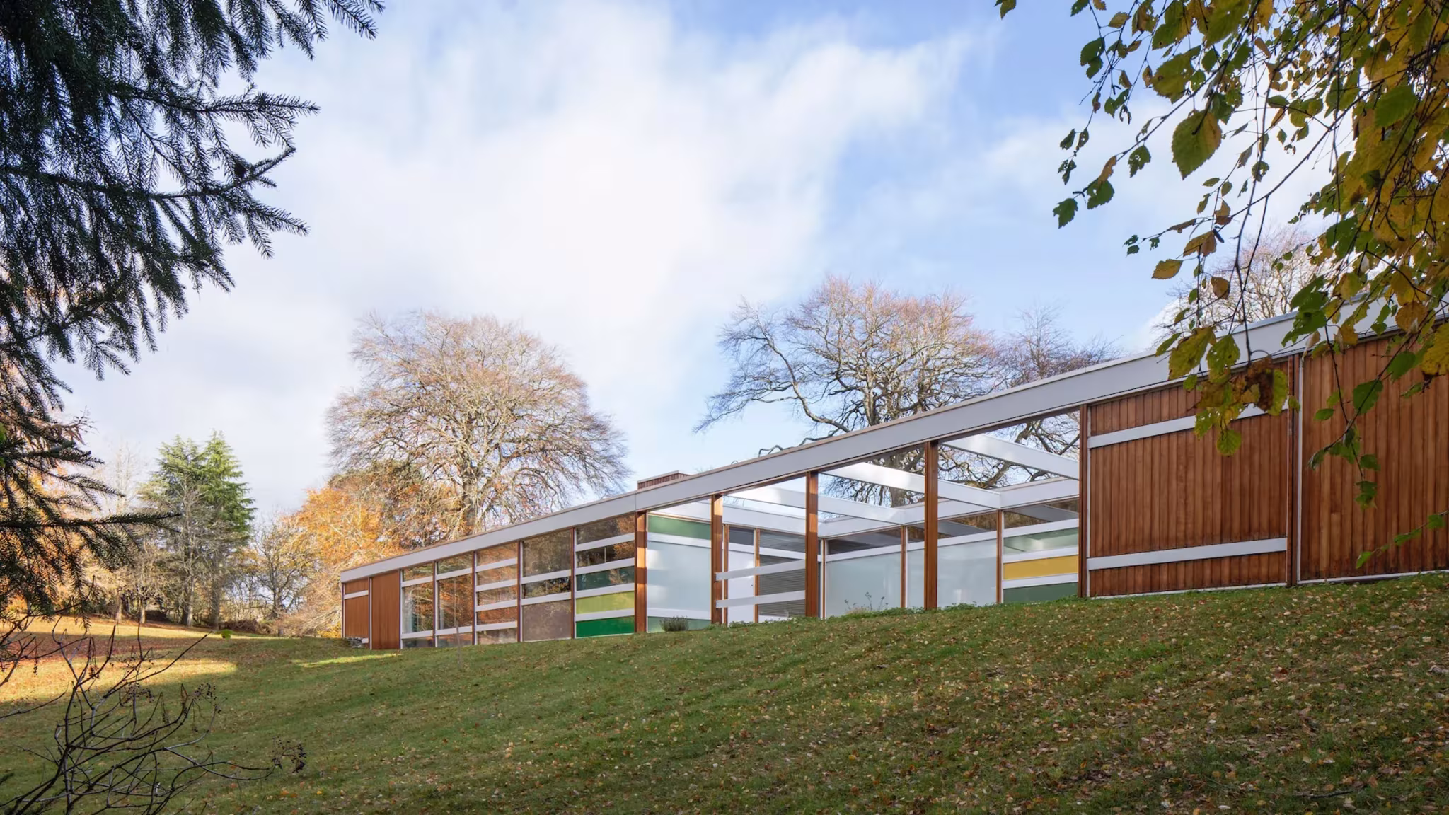 Casa High Sunderland, pabellón bajo con paneles de colores y madera sobre una pradera con árboles