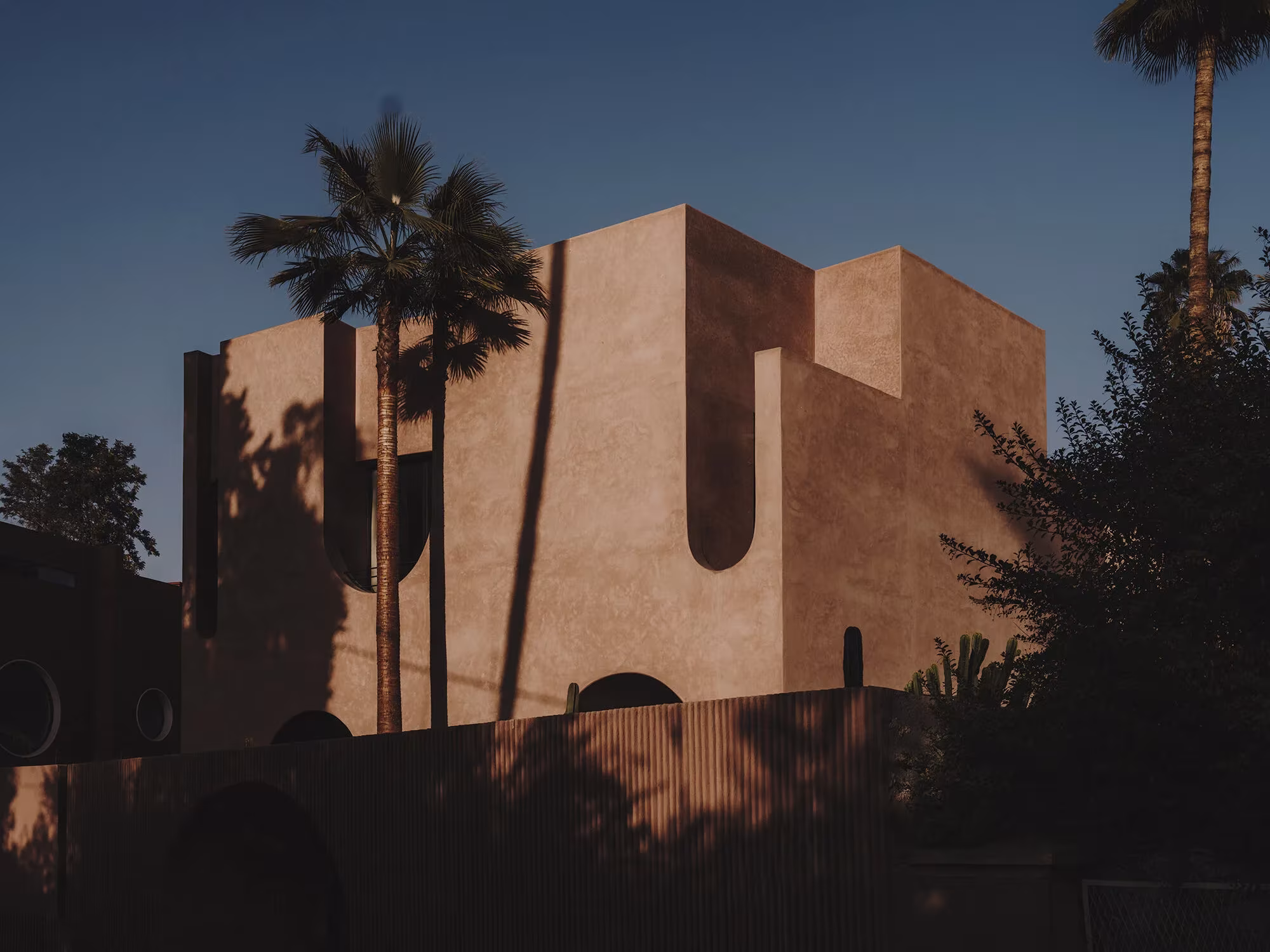 Maison Brummell Majorelle al atardecer, volumen de tierra con aberturas curvas entre palmeras