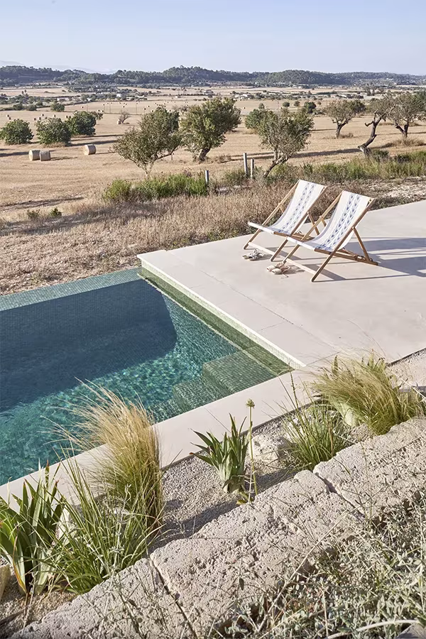 Piscina de la Casa Palerm con dos tumbonas de lona y gramíneas, frente a un paisaje de olivos y campos secos