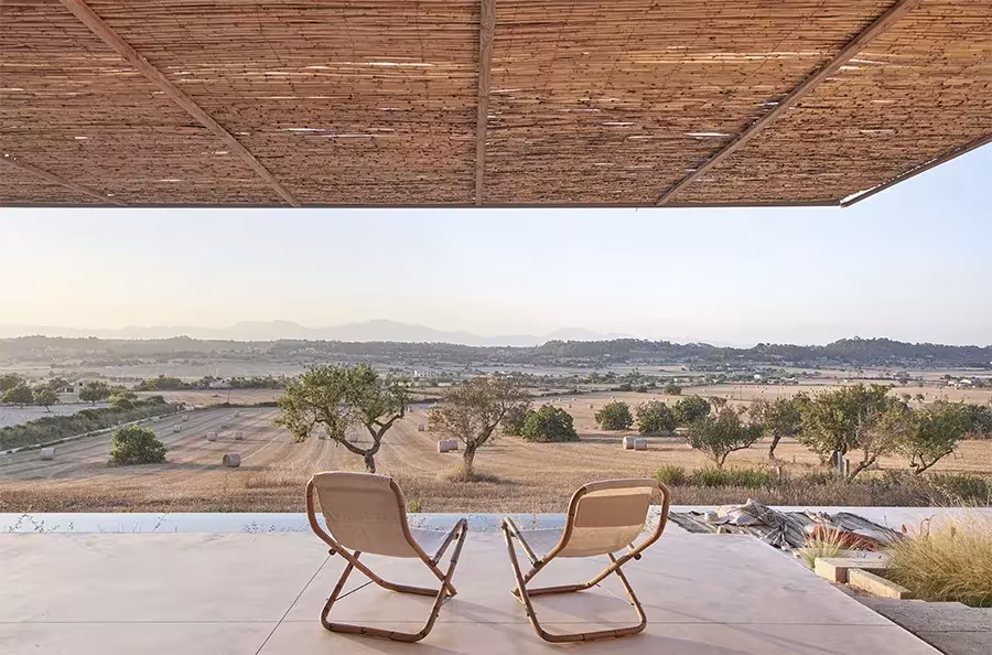 Dos butacas de madera bajo la pérgola de cañizo de la Casa Palerm, mirando a la llanura con árboles