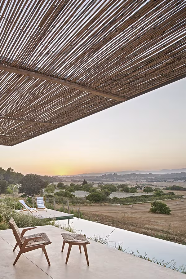 Terraza de la Casa Palerm con butaca y reposapiés junto a la piscina, bajo cañizo y con el sol poniéndose