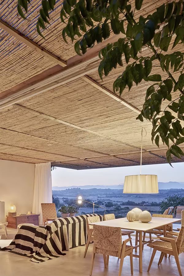 Comedor de la Casa Palerm con mesa de madera, lámpara blanca y sofá de rayas abierto al paisaje