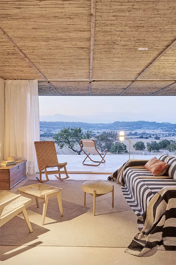 Salón de la Casa Palerm con sofá de rayas blancas y negras, butacas de cuerda y vistas al campo