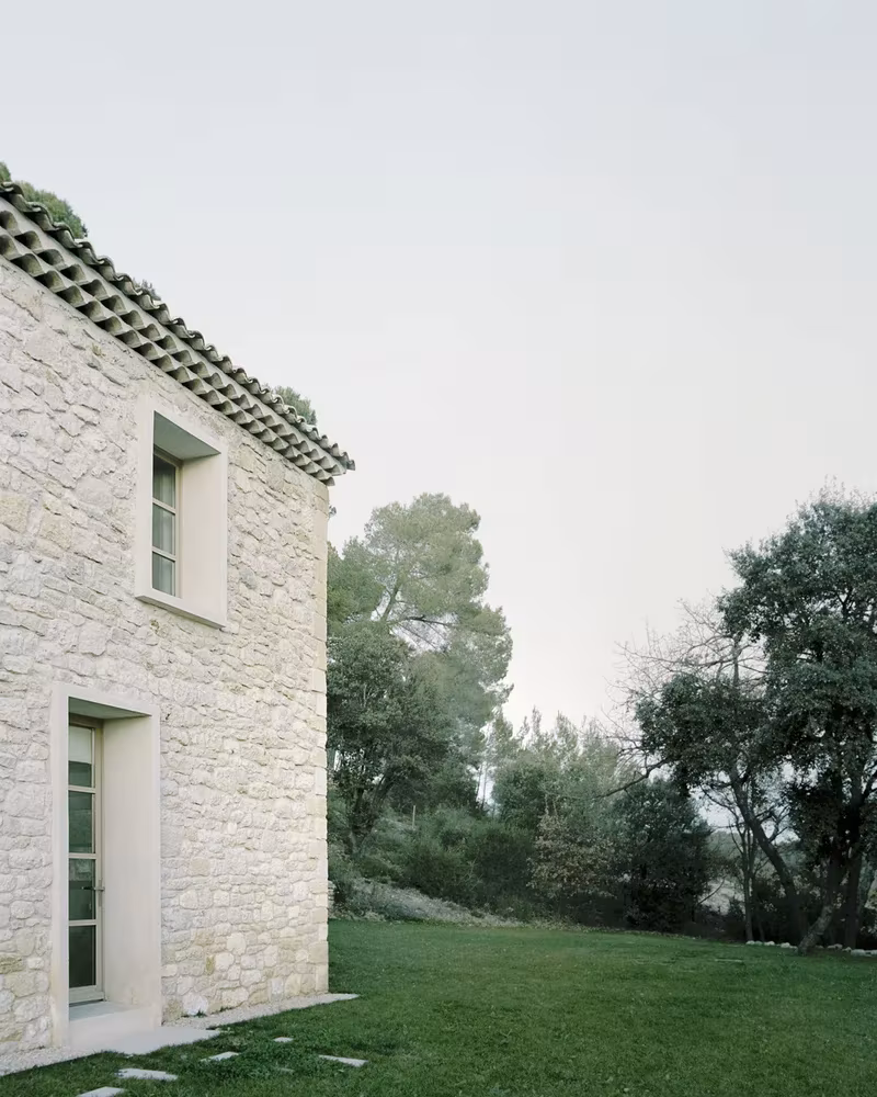 Esquina de la Casa MA con muro de piedra, cubierta de teja y ventana frente al jardín de césped
