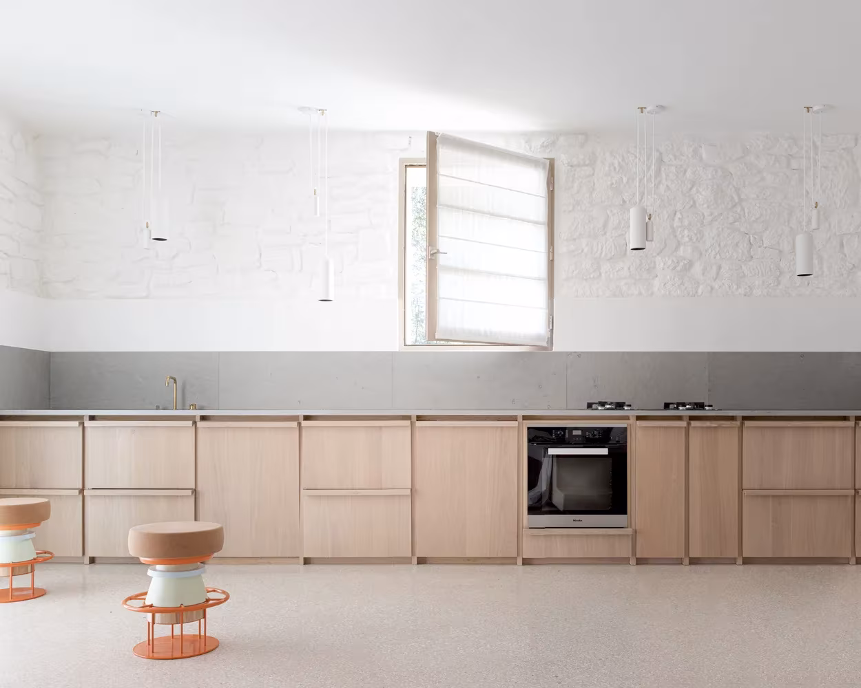 Cocina de madera clara bajo un muro de piedra encalada con ventana batiente en la Casa MA, Vaucluse