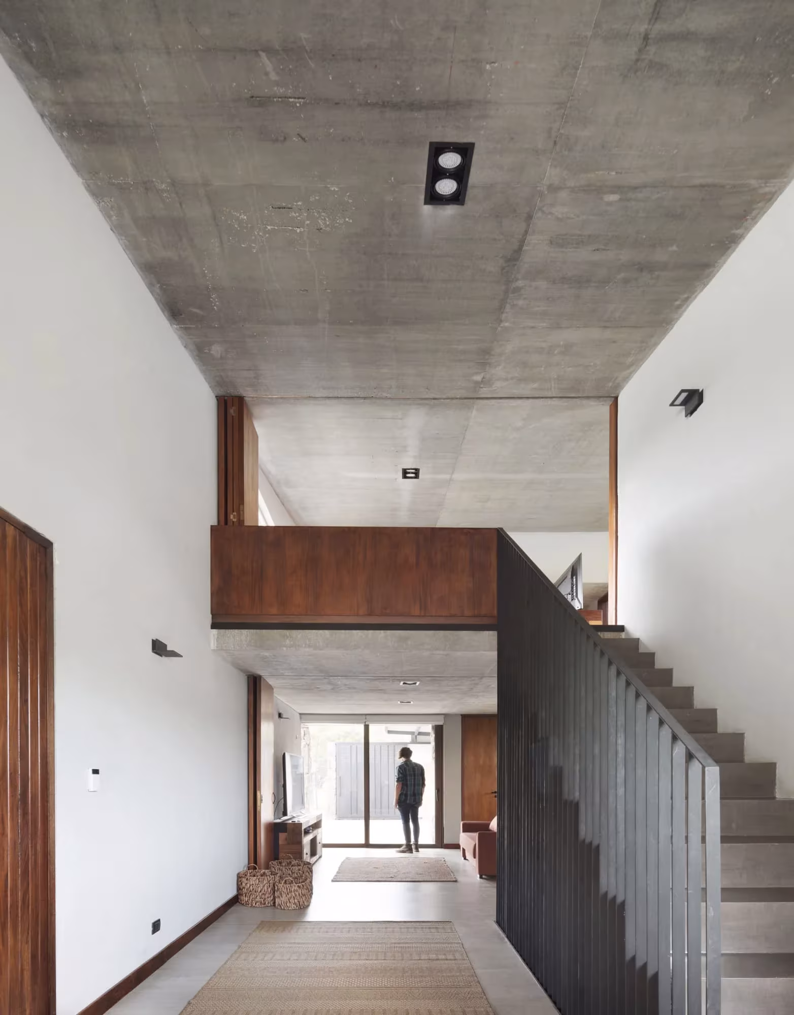 Doble altura con techo de hormigón, escalera y pasarela de madera abierta al lago en la Casa MM