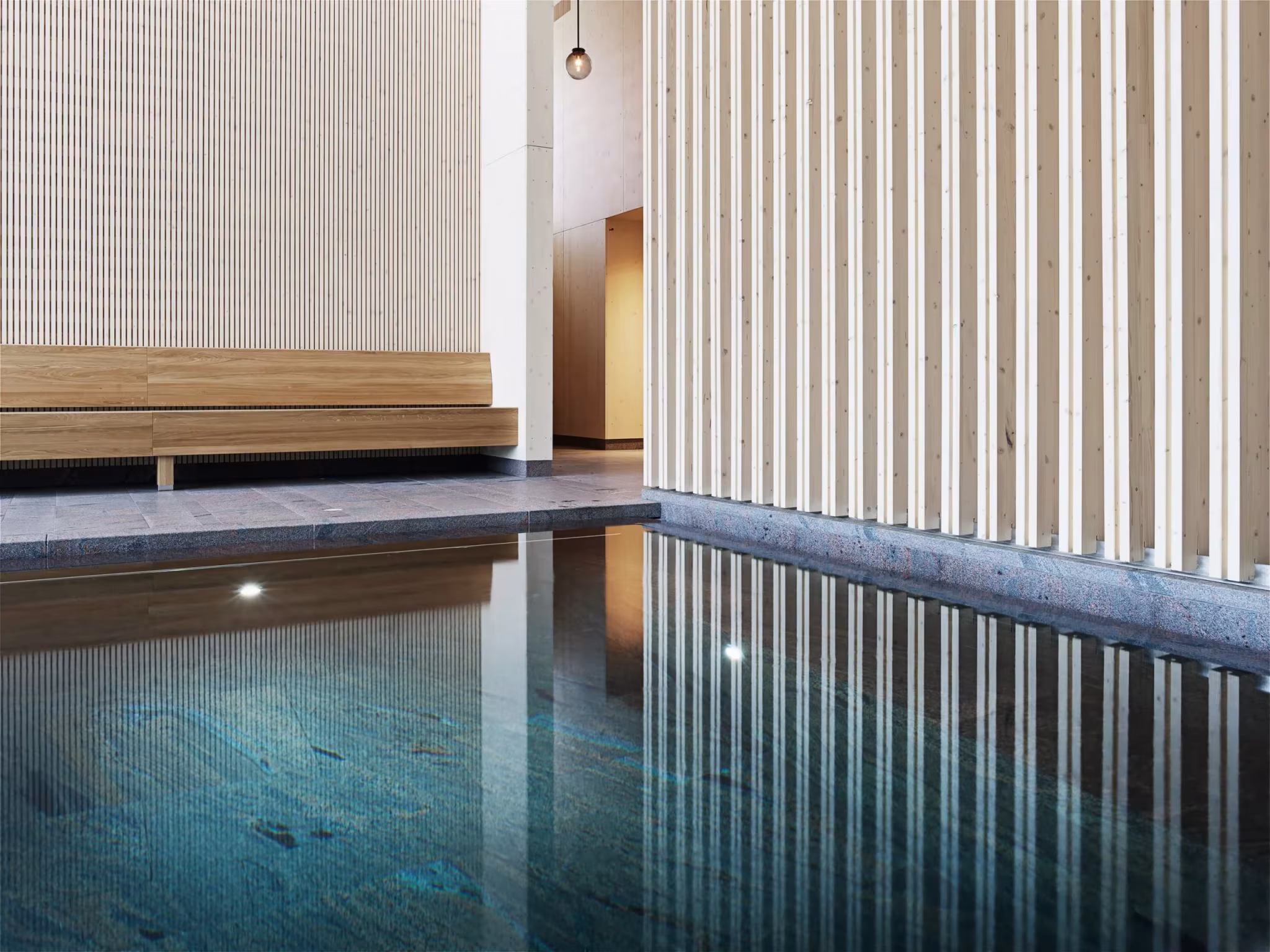 Lámina de agua del Andrum Spa reflejando listones verticales de madera y un banco iluminado