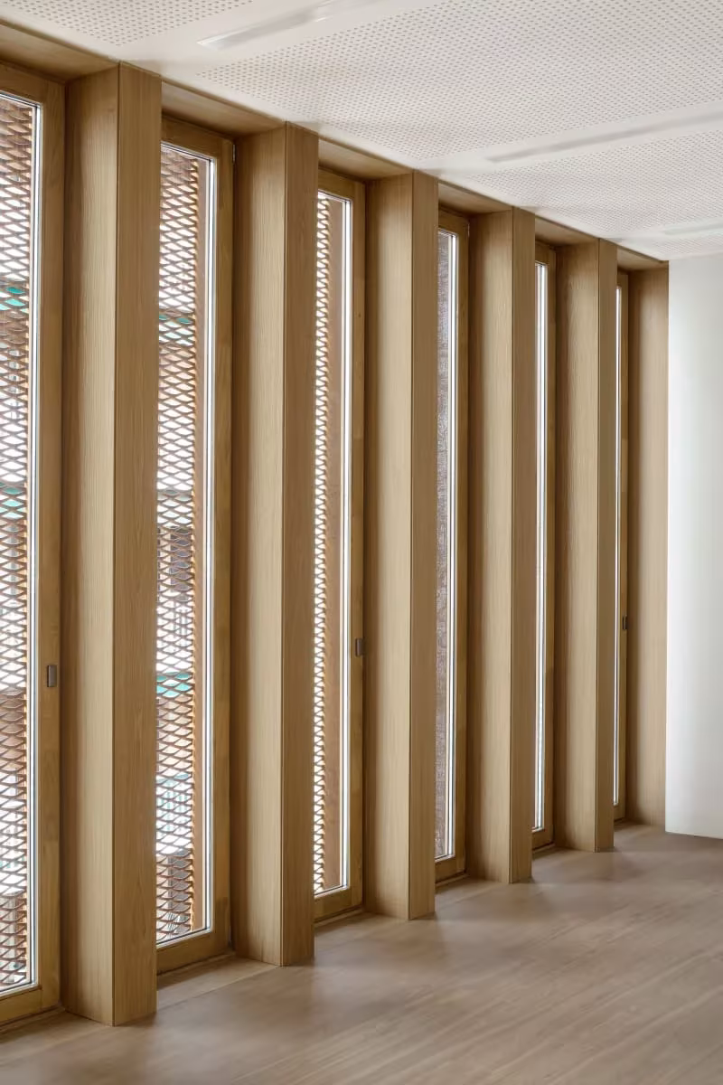 Aula blanca de la Escuela de Música de Zubiaur con ventanas verticales estrechas y celosías de madera