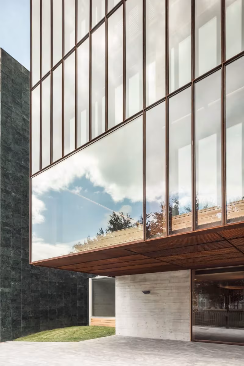 Esquina acristalada de la Escuela de Música de Zubiaur que refleja nubes, volada sobre una base de hormigón