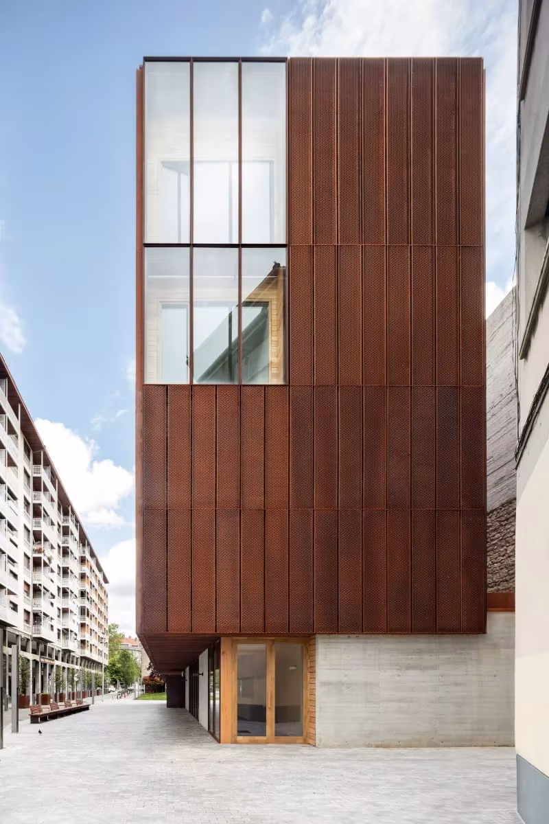 Fachada lateral de la Escuela de Música de Zubiaur con paneles de acero corten y vidrio entre edificios de viviendas