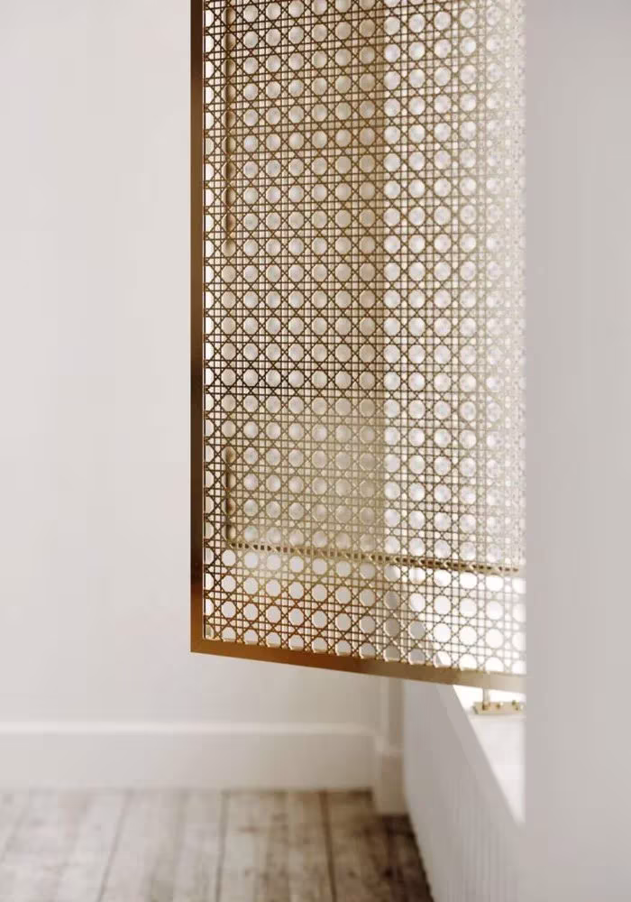 Celosía dorada calada colgada junto a una ventana en un interior blanco del proyecto Sense