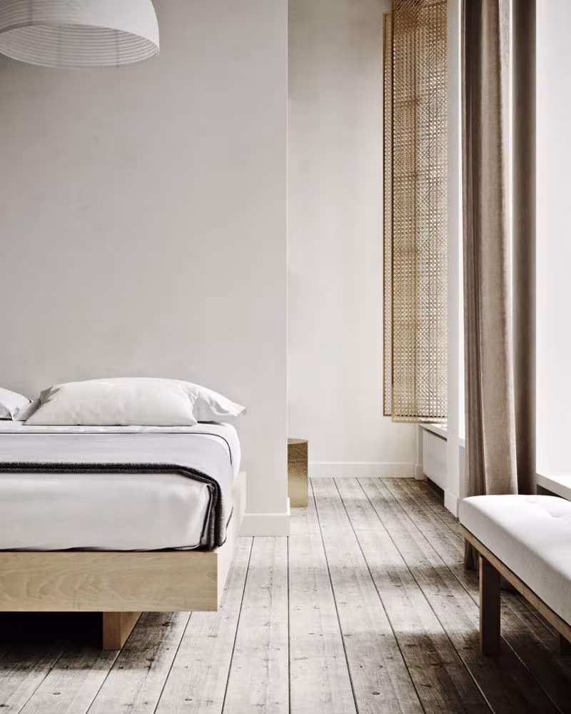Dormitorio del proyecto Sense con cama blanca sobre base de madera, banco bajo y cortinas de lino