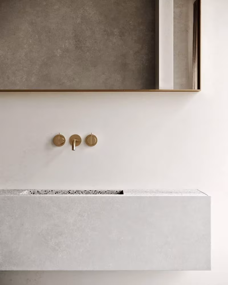 Lavabo de piedra clara volado con grifería dorada empotrada y espejo enmarcado en latón