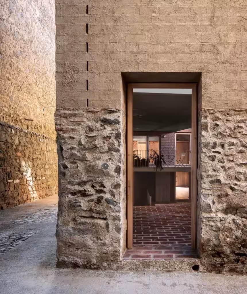Acceso a las Bodegas Clos Pachem por un hueco en un muro de piedra y tapial, con interior iluminado