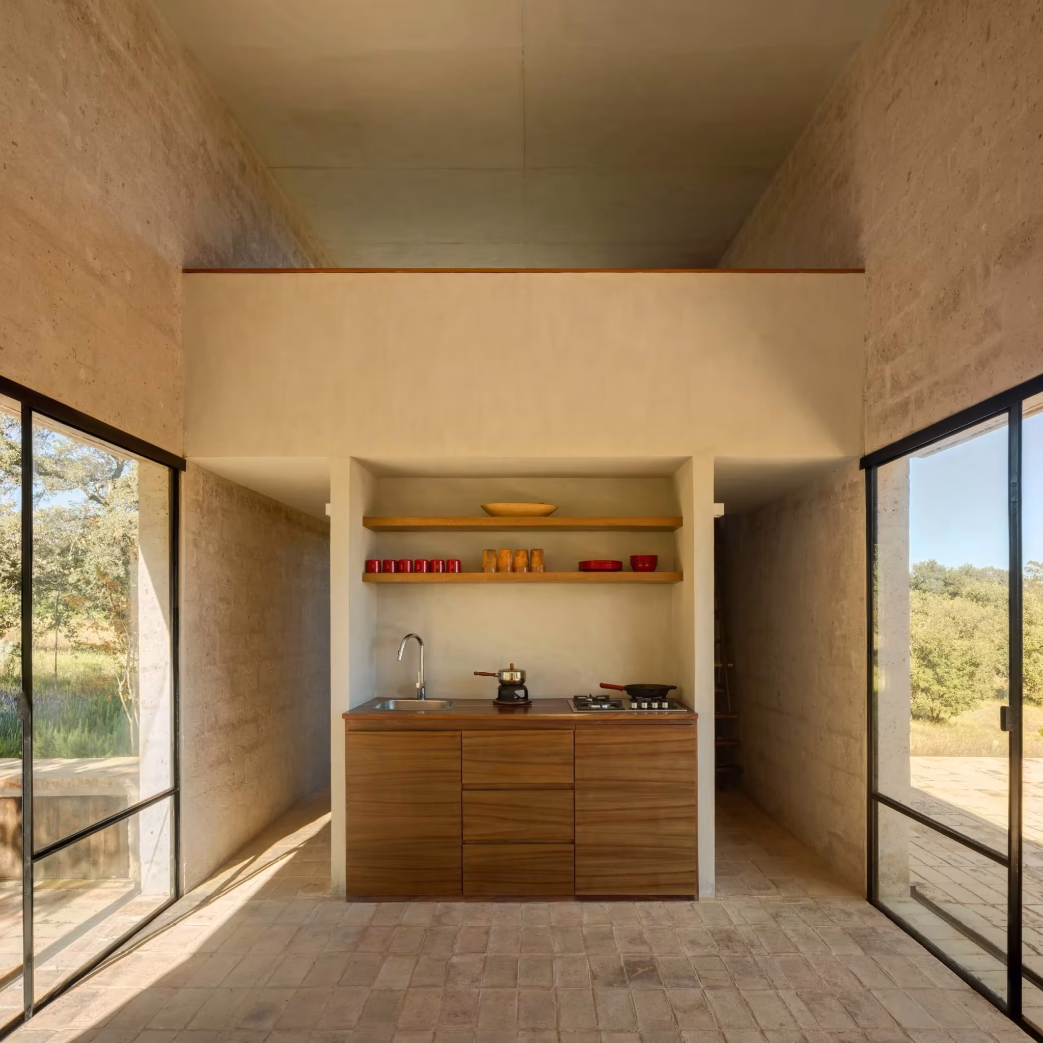Cocina compacta de madera del refugio de Aculco empotrada en un nicho de piedra entre dos ventanales