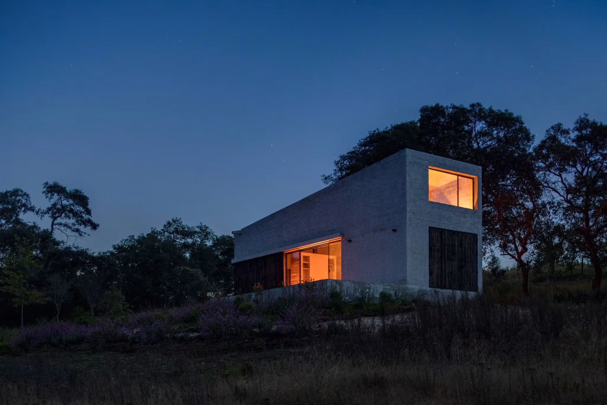 Refugio de Aculco al anochecer con sus ventanas iluminadas sobre una loma entre árboles