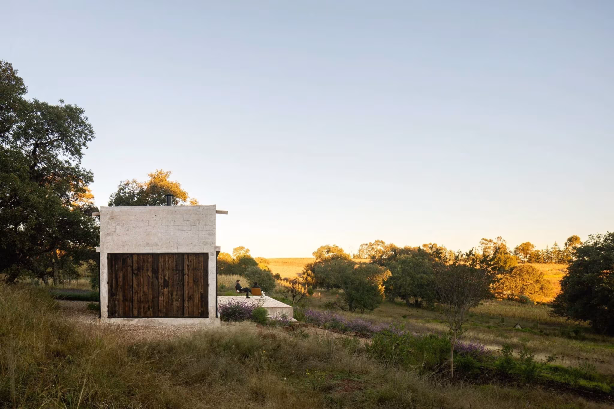 Refugio de Aculco al atardecer, volumen de piedra con puertas de madera en un prado dorado