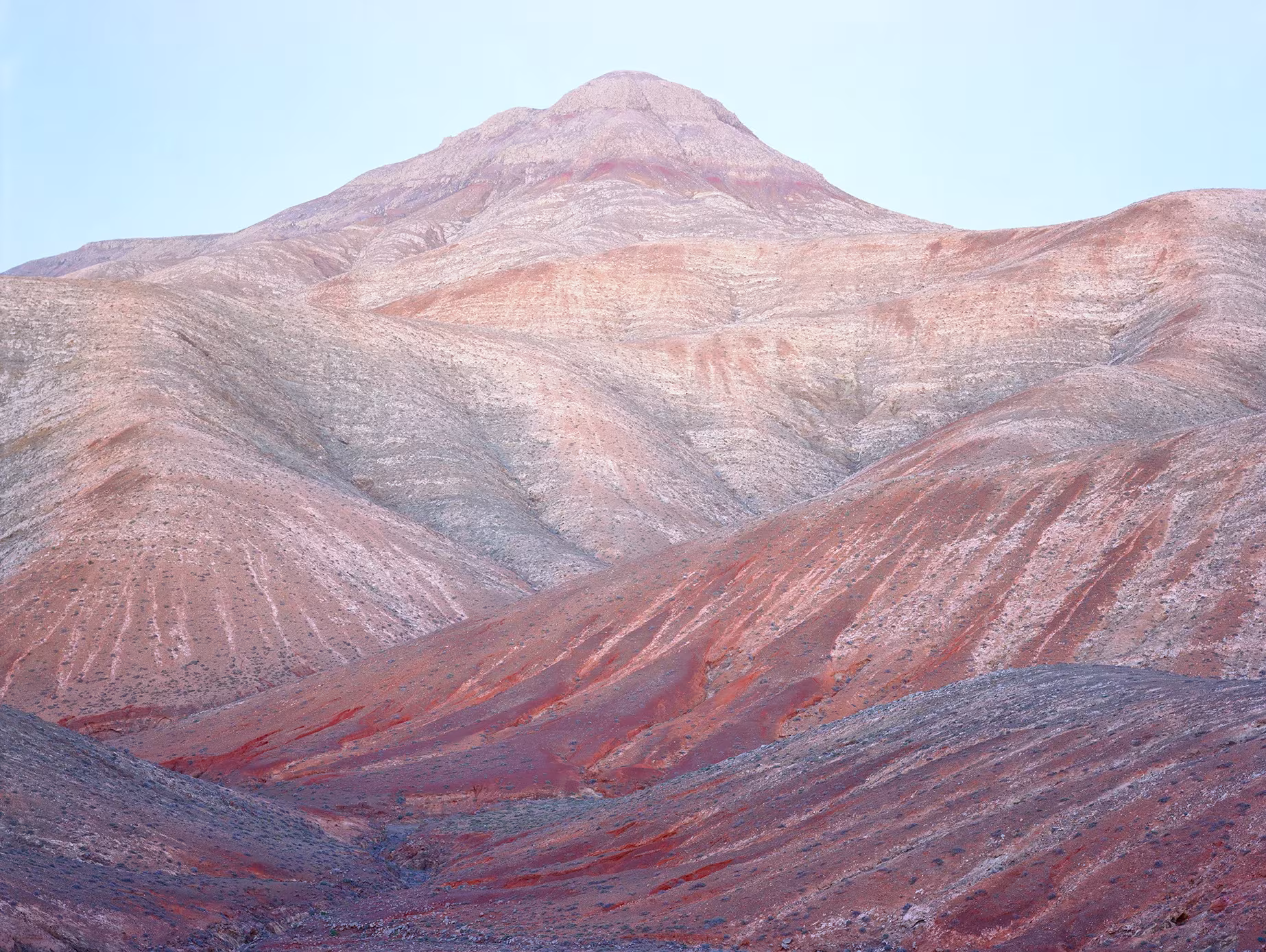 Montaña de laderas rojizas y grises en un paisaje desértico fotografiado por Luca Tombolini