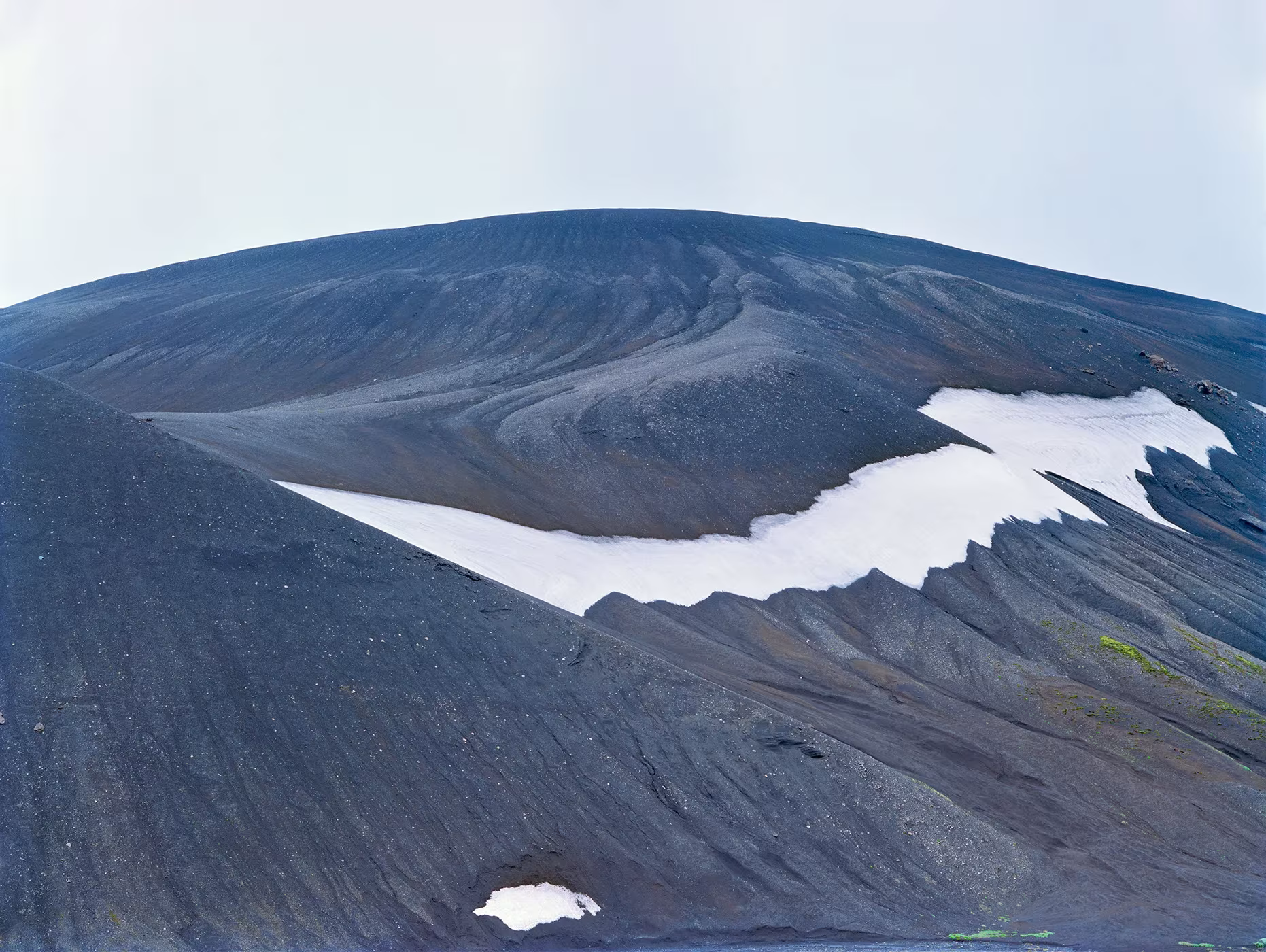 Ladera de ceniza negra con vetas de nieve blanca bajo un cielo claro, fotografía de Luca Tombolini