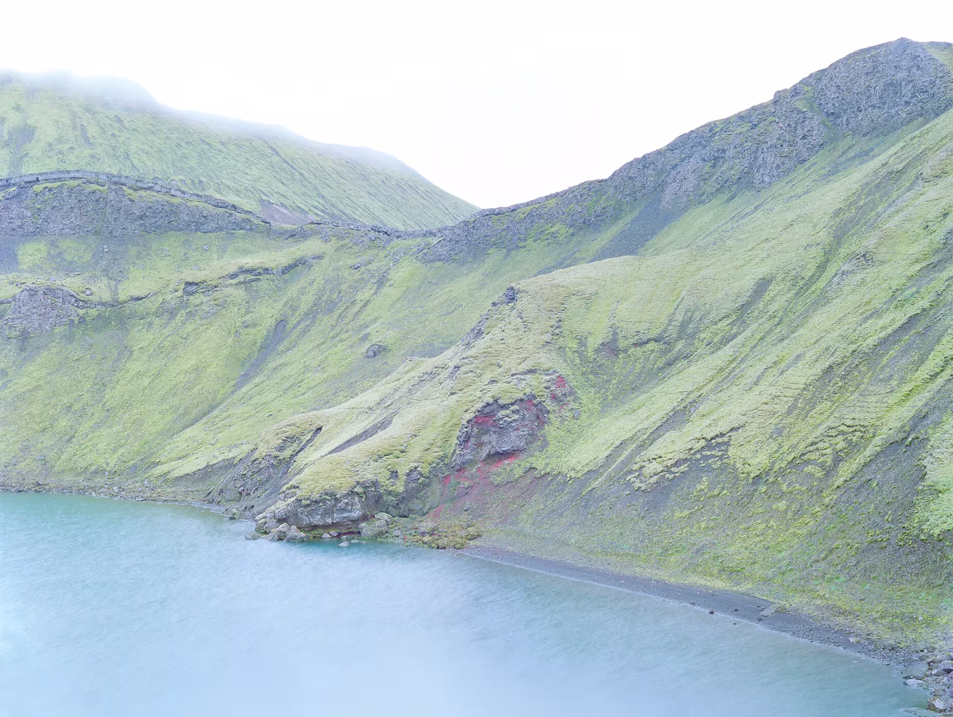 Laderas verdes que caen sobre un lago azul claro bajo la niebla, fotografía de Luca Tombolini