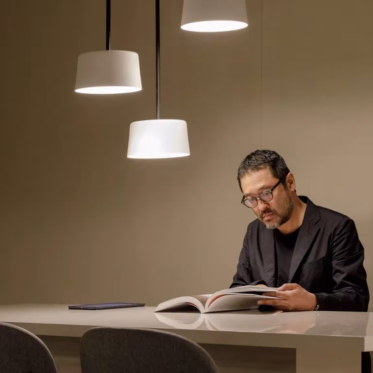 Hombre leyendo un libro sobre una mesa bajo lámparas colgantes Tube de Vibia
