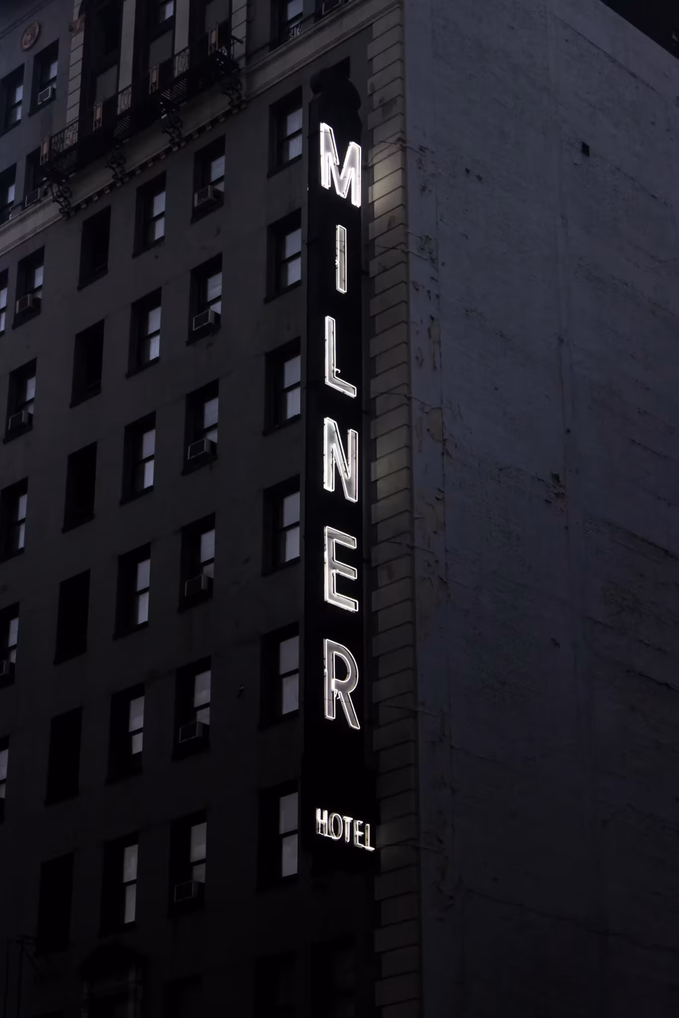 Rótulo vertical del Milner Hotel sobre una fachada oscura de ventanas, fotografía de Guillermo Santos