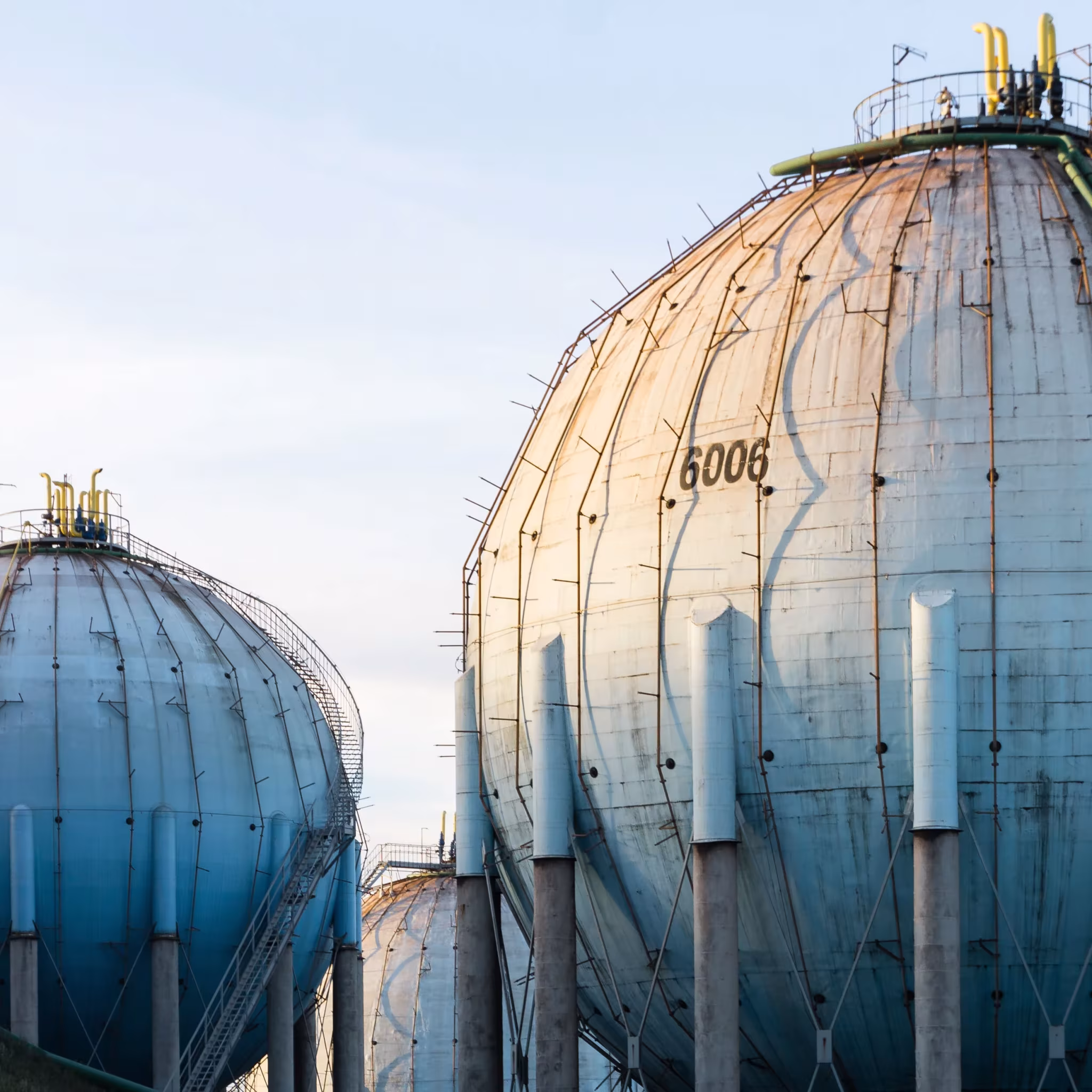 Depósitos esféricos de gas con manchas de óxido y columnas bajo un cielo azul, de Guillermo Santos