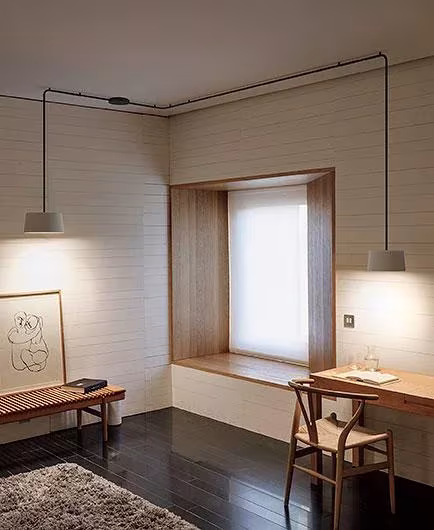 Rincón con ventana, banco de madera y escritorio bajo dos lámparas Tube de cableado negro