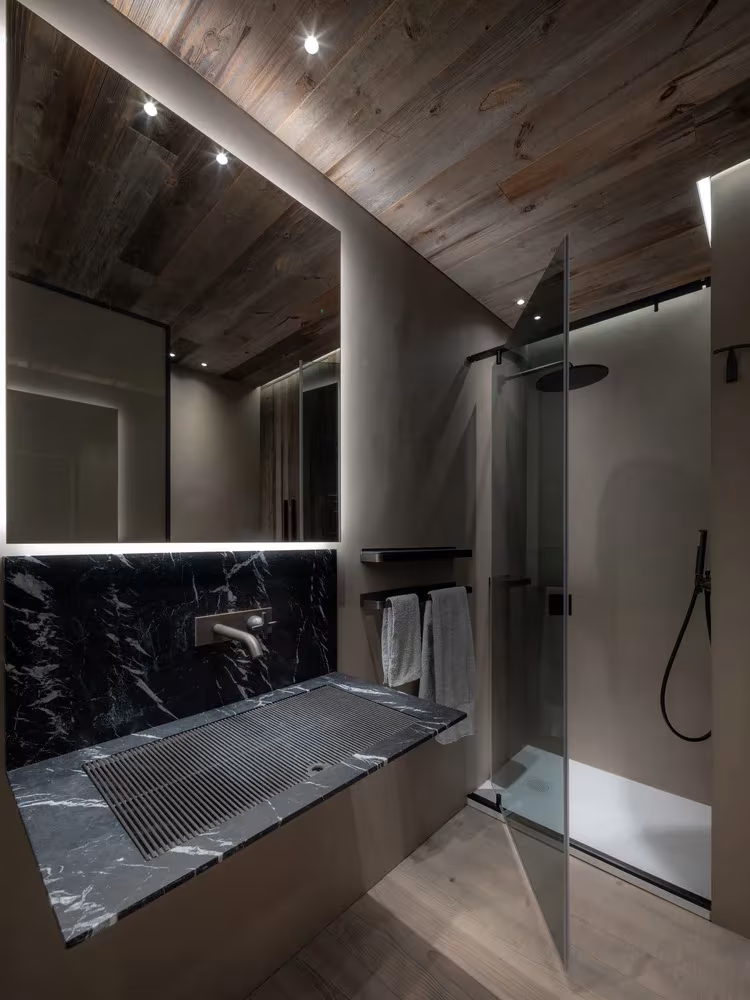 Baño de Casa Cortina de Outline Studio 74 con mármol negro, ducha de vidrio y techo de madera oscura