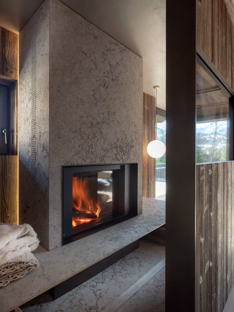 Chimenea encendida empotrada en un muro de piedra dolomítica en Casa Cortina, junto a una lámpara de globo