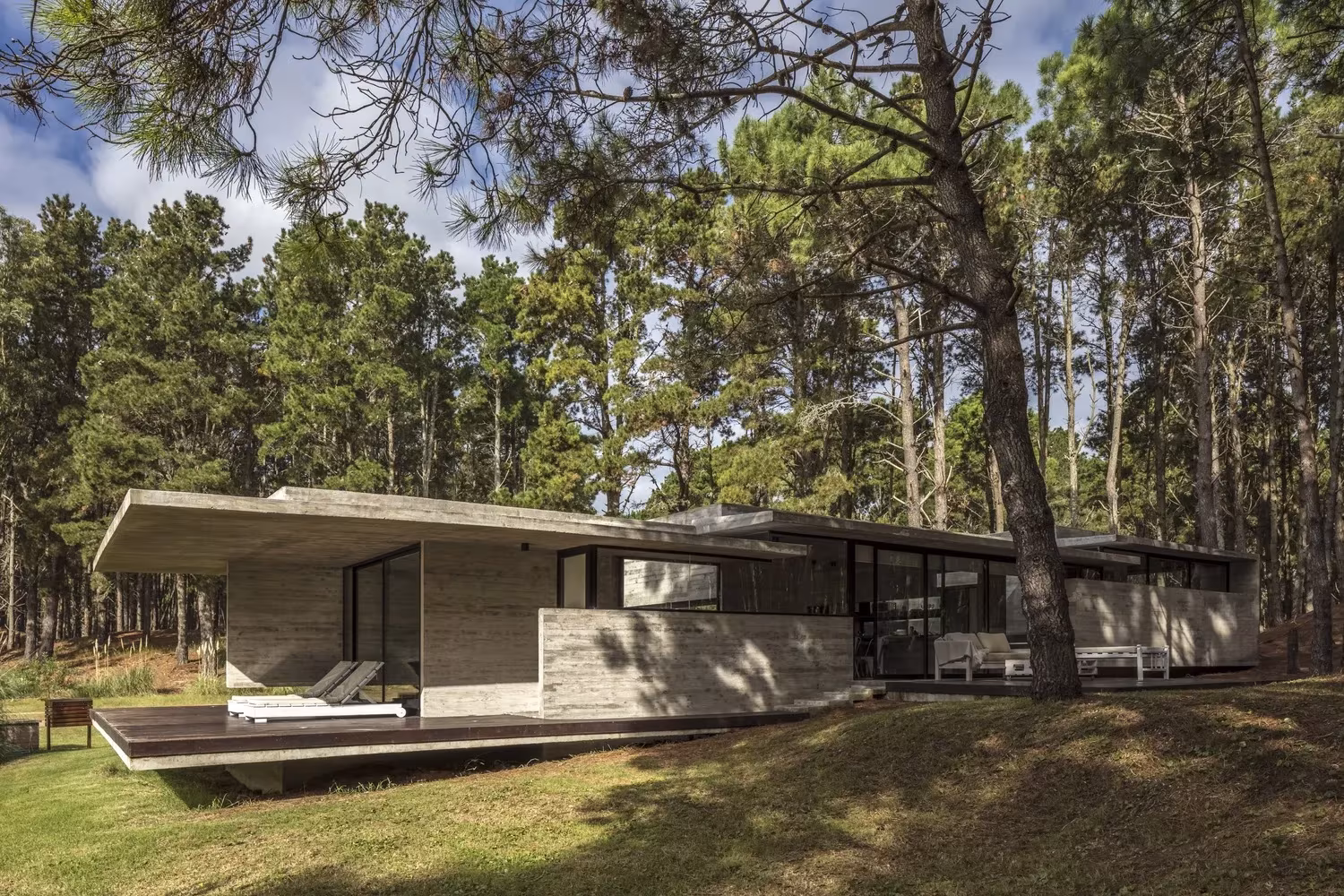 Casa Bosque de Besonías Almeida con cubierta plana de hormigón y terraza de madera bajo altos pinos