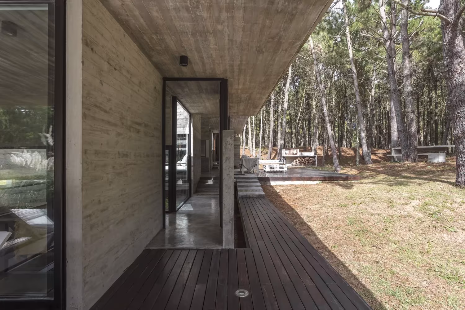 Galería exterior de la Casa Bosque con suelo de tablas, techo de hormigón y vista al pinar