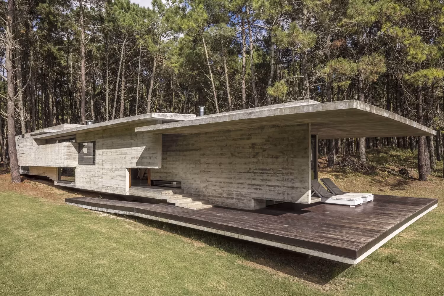 Casa Bosque con dos cubiertas planas superpuestas y terraza de madera volada sobre el césped