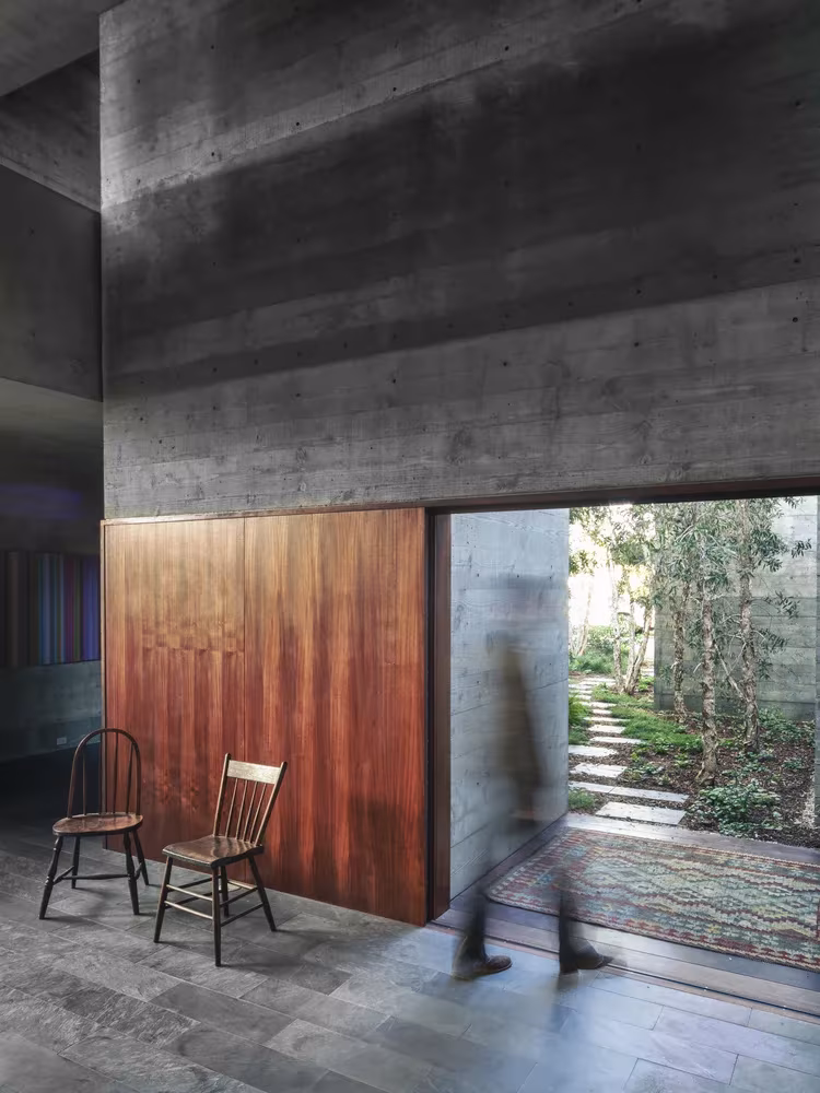 Puerta corredera de madera junto a dos sillas y un patio ajardinado al fondo en la Casa Phoenix