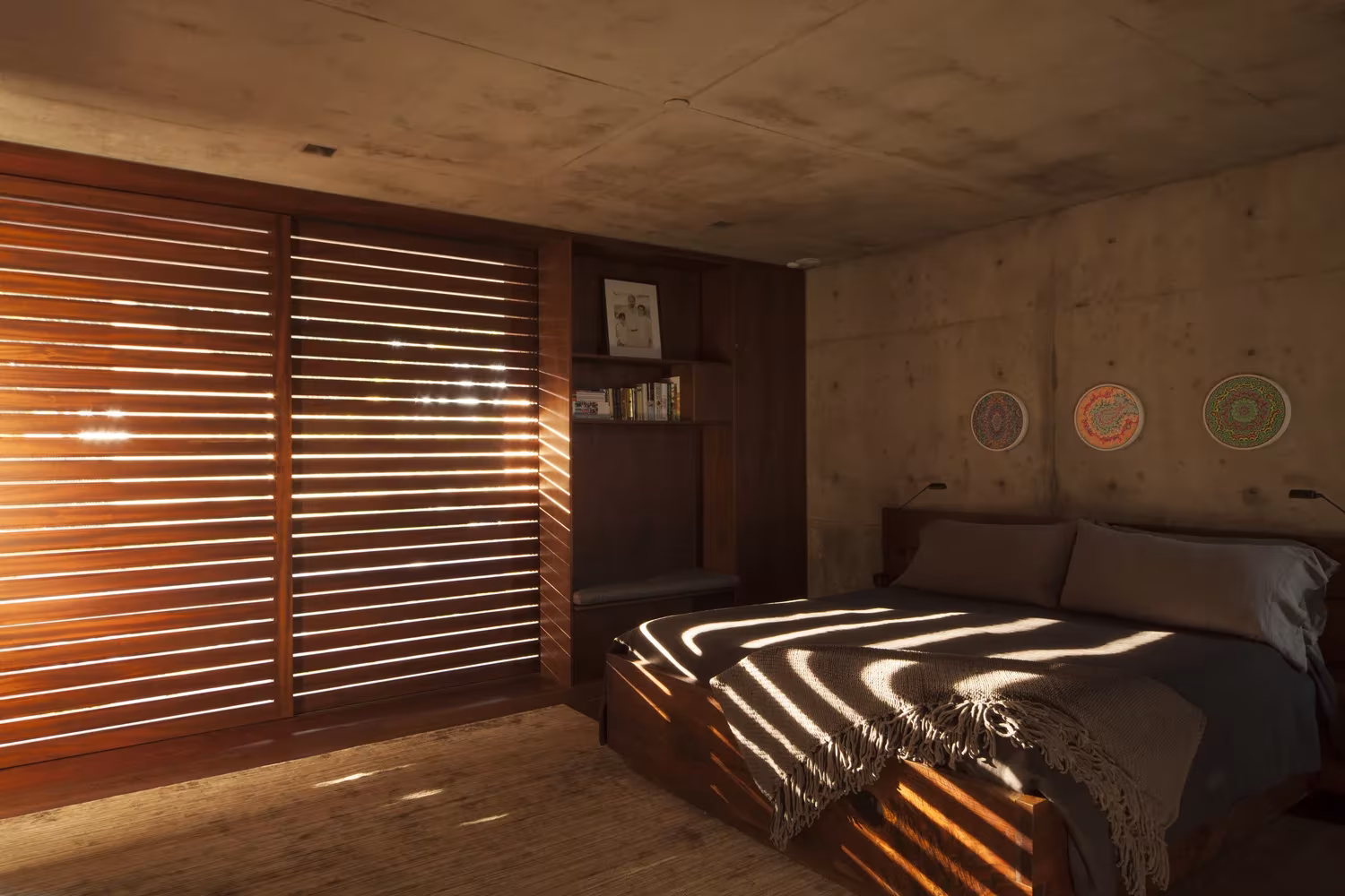 Dormitorio con contraventanas de lamas de madera que dibujan sombras sobre la cama en la Casa Phoenix